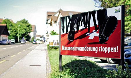 3 fold Nazi poster
                            of SVP in 2011 "stop mass
                            immigration" with black boots on a
                            Swiss flag at an entrance of a village
